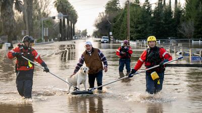 San Diego firefighters help Humberto Maciel rescue his dog from his flooded home in Merced. AFP