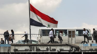A Syrian flag flies as people cross the Hafez Al Assad bridge over the Barada river in the centre of Damascus on April 14, 2024. AFP