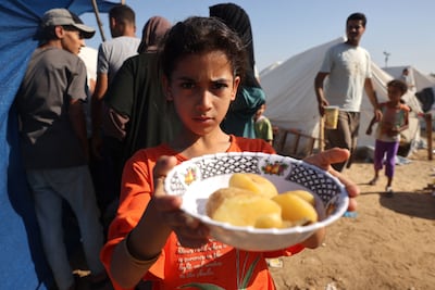 A displaced Palestinian girl shows her plate of food collected at a food distribution point as she and her family shelter in tents set up in a UN-run centre, in Khan Younis, in southern Gaza, on October 26. AFP