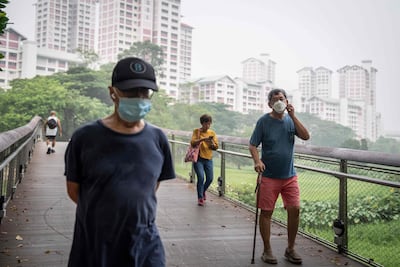 People wearing face masks walk past a government public housing apartment in Singapore. AFP