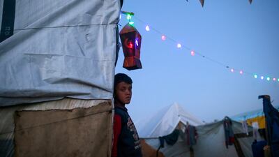 A displaced Palestinian child outside his family's shelter as lanterns and Ramadan accessories decorate the tents. EPA
