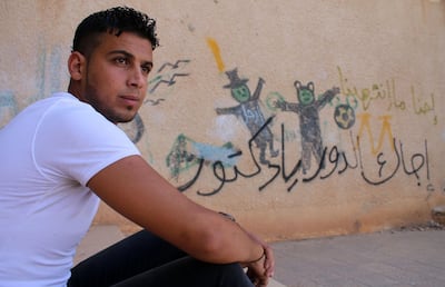 Moawiya Sayasina, the Syrian activist who started scribbling anti-Assad slogans in 2011, sits next to a graffiti drawn on the wall of a schoolyard reading in Arabic "Your turn, Doctor", in a rebel-held neighbourhood in the southern Syrian city of Daraa. AFP