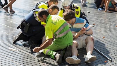 A person is helped by Spanish policemen and two men after a van ploughed into the crowd, killing at least 13 people and injuring around 100 others on the Rambla in Barcelona on August 17, 2017. A driver deliberately rammed a van into a crowd on Barcelona's most popular street on August 17, 2017 killing at least 13 people before fleeing to a nearby bar, police said. Officers in Spain's second-largest city said the ramming on Las Ramblas was a "terrorist attack". The driver of a van that mowed into a packed street in Barcelona is still on the run, Spanish police said. / AFP PHOTO / Nicolas CARVALHO OCHOA