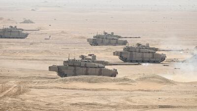A fleet of tanks roll over the desert dunes of an Abu Dhabi training field.