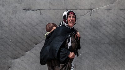 A displaced Syrian Kurdish woman from the city of Ras al-Ain carries a child on her back as she walks throught the al-Talaeh displacement camp in Hasakeh, northeastern Syria. AFP