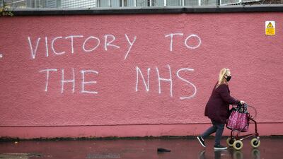 FILE - In this Tuesday, Dec. 8, 2020 file photo, a woman walks past graffiti with the words Victory to the NHS (National Health Service) on a wall at the Royal Victoria Hospital, one of several hospitals around Britain that are handling the initial phase of a COVID-19 immunization program, in West Belfast, Northern Ireland. Britain races to vaccinate more than 15 million people by mid-February, and in an effort to ensure vaccines get to the right places at the right times, along with the syringes, alcohol swabs and protective equipment needed to administer them, the government has called in the army. (AP Photo/Peter Morrison, File)