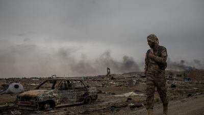 A Syrian Democratic Forces (SDF) fighter walks past destroyed vehicles in the final ISIS encampment on March 24, 2019 in Baghouz, Syria. Getty Images.