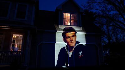 An image of veteran Stephen Kulig, who died from the COVID-19 virus at the age of 92, is projected onto the home of his daughter, Elizabeth DeForest, as she looks out the window of a spare bedroom as her husband, Kevin, sits downstairs in Chicopee, Massachusetts, USA. AP Photo
