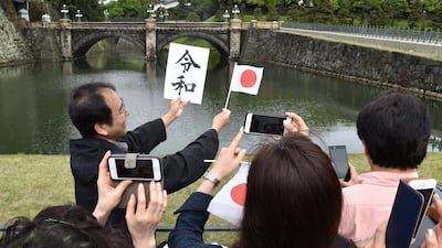 Visitors take photos of a man holding up a Japanese flag along with a card showing the characters for the new "Reiwa" era to mark the new emperor's reign, outside the grounds of the Imperial Palace in Tokyo. Japan's new Emperor Naruhito formally ascended the Chrysanthemum Throne on May 1, a day after his father abdicated from the world's oldest monarchy and ushered in a new imperial era. AFP