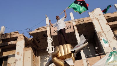 A Libyan rebel fighter waves their flag on top of the monument that remebers the bombing by US forces in 1986, inside the Bab al-Aziziya compound, the main stronghold of Gaddafi, in Tripoli, Libya, on 23 August 2011. Libyan rebels fired celebratory rounds???