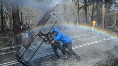 Migrants take cover behind a wooden board as Greek police uses water cannons to block them trying to break fences in the Turkey-Greece border province of Edirne. AFP