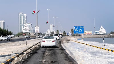 Vehicles drive on a debris-laden coastal road in Kalba on Tuesday.