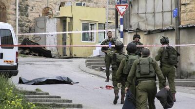Israeli soldiers stand near the body of a Palestinian man who was shot in the head and killed while lying wounded on the ground after an alleged stabbing attack in the West Bank city of Hebron on March 24, 2016. AP Photo