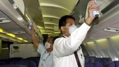 Maintenance crew members wearing preventative masks spray a place to kill microscopic stowaways and mosquitos.