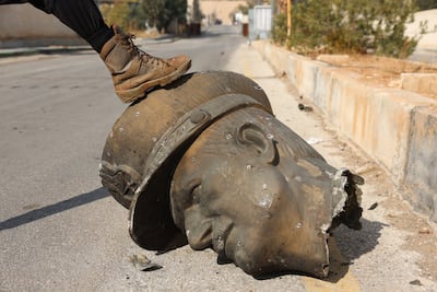 An opposition fighter steps on the head of a statue of late Syrian president Hafez Al Assad at Mazzeh Military Airport, Damascus, on December 12. EPA