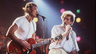 (FILES) This file photo taken on April 2, 1985 shows French singers Eddy Mitchell (R) and Johnny Hallyday performing at the stadium om Bourges during the 9th edition of the Printemps de Bourges. France's best-known rock star Johnny Hallyday has died aged 74 after a battle with lung cancer, his wife Laeticia told AFP on December 6, 2017. / AFP PHOTO / Frank PERRY