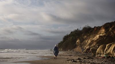 A person walks at high tide near eroding cliffs along the Pacific Ocean coastline in Del Mar, California. AFP