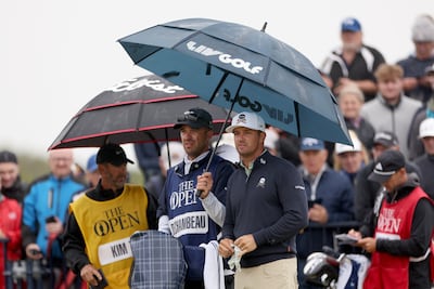 Bryson DeChambeau and his caddie Greg Bodine look on from under an umbrella on the 17th tee on day one of The 152nd Open championship at Royal Troon on July 18, 2024, in Troon, Scotland. Getty Images