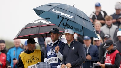 Bryson DeChambeau and his caddie Greg Bodine look on from under an umbrella on the 17th tee. Getty Images
