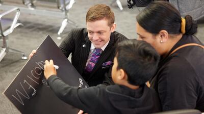 A member of an Air New Zealand flight crew assists people writing a message on a welcome board at Auckland International Airport in New Zealand. Bloomberg