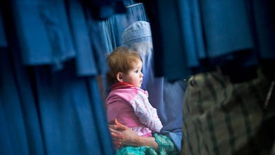 An Afghan woman waits with her child in front a changing room to try on a new burqa.