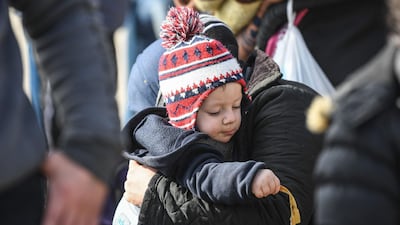 A child plays with a piece of banana's skin as he is carried in the arms of a migrant woman walking towards the Pazarkule border gate in Edirne on March 4, 2020, during their journey to try to enter Europe. Turkish officials claimed on March 4, 2020 that one migrant was killed by Greek fire on the Turkey-Greece border where thousands of migrants have massed since last week. But on the other side Greece "categorically" denied claims by Turkey that it had fired live bullets against migrants on the border, with several allegedly injured and one later dying. / AFP / Ozan KOSE