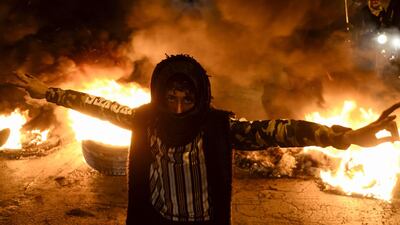 A masked anti-government protester flashes the victory gesture as he stands before flaming tyres at a make-shift roadblock in the central Iraqi holy shrine city of Najaf. AFP