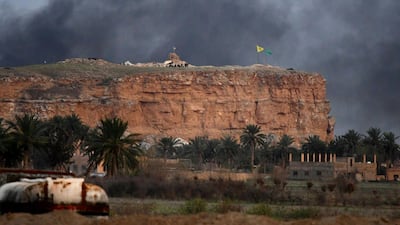 Smoke rising over the village of Baghouz in the eastern Syrian province of Deir Ezzor, with the flags of the Kurdish People's Protection Units (Yellow) and Women's Protection Units (Green) seen flying at one of their positions in the background. AFP
