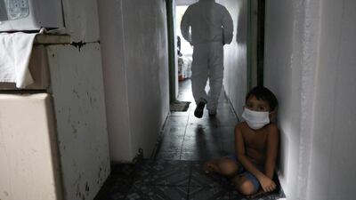 A kid looks on as a municipal healthcare worker walks after examining the body of Shirlene Morais Costa, who died at home at the age of 53 after reporting symptoms consistent with Covid-19, in Manaus, Brazil. Reuters