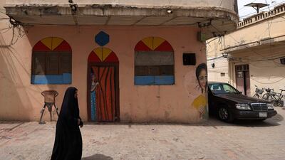 A woman walks past a mural of a girl peeping from behind a curtain