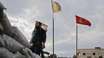 A fighter from Faylaq al-Sham is seen holding a Kalashnikov rifle as he stands in front of the flags at a position in the village of Kiridiyah. AFP