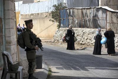 An Israeli soldier stands watch as Palestinian women and school children return home in the Tel Rumeida neighbourhood. Heidi Levine for The National
