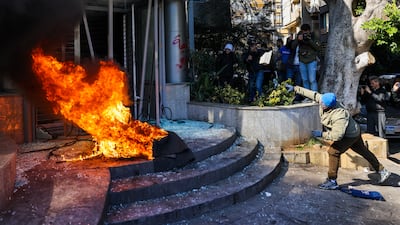 A protester throws a brick at a bank after setting fire to tyres during a demonstration in Beirut on February 16, 2023. Dozens of angry Lebanese demonstrators attacked several banks on February 16 after the local currency dropped in value to a record low in as part of a deepening economic crisis, AFP photographers said. (Photo by Joseph EID / AFP)