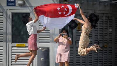 Women holding the Singapore national flag pose for a photograph at the Merlion Park to mark the 55th National Day celebrations in Singapore. AFP