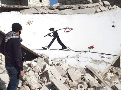 Abu Malek Al Shami stands in front of one of his murals painted on the collapsed roof of a building in Idlib, Syria. Abd Almajed Alkarh for The National.