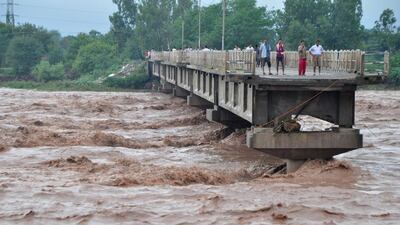 Indian villagers look on by the edge of a missing section of a bridge across the overflowing Tawi river that was swept away during floods. AFP Photo