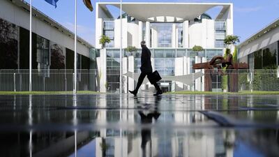 A man is reflected in a puddle from rain as he walks in front of the chancellery with the office of German Chancellor Angela Merkel in Berlin. Markus Schreiber / AP Photo