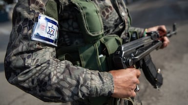 A member of the National Guard in Sweida, whose uniform displays the Israeli flag and a portrait of Druze leader Sheikh Hikmat Al Hijri. Hasan Belal for The National