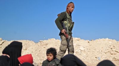 A member of the Syrian Democratic Forces walks past women and children waiting. AFP