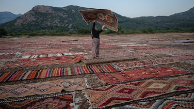 TOPSHOT - A worker holds an handwoven carpet laid out in an open field to soften its colours under sizzling sun in Dosemealti district in Antalya on July 22, 2025. Thousands of carpets and kilims spread out in the sun form a festive and colourful patchwork on the outskirts of Antalya, the large coastal tourist city in southern Turkey. From June to September, in the harvested fields cleared of stubble, traders bring their cargoes to age in the sun, tempering the overly bright hues of their natural colours under its rays and ridding them of any unwanted elements. (Photo by Ozan KOSE / AFP)