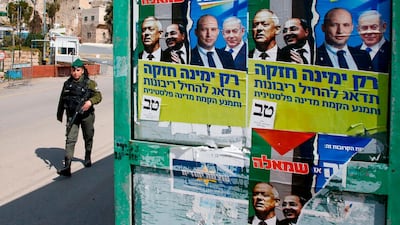A member of the Israeli security forces walks past election posters of Israel's Blue and White political alliance leader Benny Gantz, Arab Israeli member of the Joint List Ahmad Tibi, Isreali Defense Minister Naftali Bennett and Prime Minister Benjamin Netanyahu in the divided West Bank town of Hebron. AFP