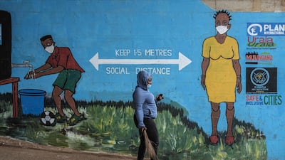 A woman wearing a face mask walks past graffiti that promotes social distancing amid the ongoing coronavirus pandemic, in Kibera, Nairobi. AFP