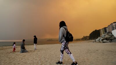 People visit the beach as a forest fire burns