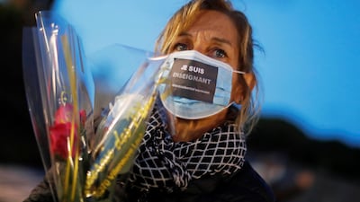 A woman wearing a protective face mask with the words "I'm a teacher" written on it pays homage to Samuel Paty, the French teacher who was beheaded on the streets of the Paris suburb of Conflans-Sainte-Honorine, as part of a national tribute, in Nice, France, October 21, 2020. REUTERS