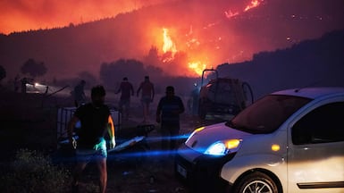 Firefighters attempt to extinguish the flames as smoke and flares rise from a forested area in Izmir, Turkey. AFP