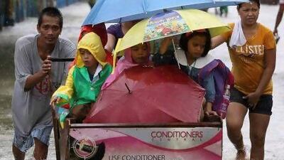 A man pushes a cart full of children as they cross a flooded road in suburban Pasig, east of Manila, yesterday.