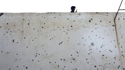 An Afghan police officer stands guard on a bullet ridden wall at a Shiite mosque where gunmen attacked during Friday prayers, in Kabul. Rahmat Gul / AP Photo