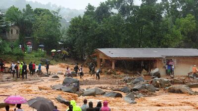 Bystanders look on as floodwaters rage past a damaged building in an area of Freetown after landslides struck the capital of Sierra Leone in mid-2017. The floods led to the deaths of more than 1,000 people. AFP