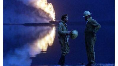 A wellhead burns out of control in 1991 as firemen contemplate the task ahead following the withdrawal of Iraqi forces from Kuwait.