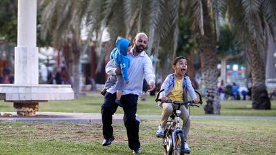 Mahmoud Al Haji teaches his son Ibrahim, 7, to ride his bike while holding his younger son Khalid, 2, at the Khalidiyah public garden in Abu Dhabi. Christopher Pike / The National